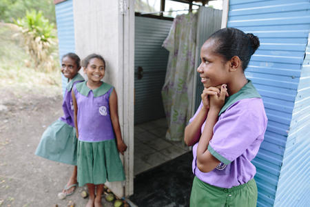 (Direita) Jemima, 12 anos, aluna do 6º ano, fora da casa de banho das meninas com as amigas (M-E) Bonni e Chanel na Escola Primária Ginigolo-Gunugau, Distrito de Rigo, Papua Nova Guiné. Outubro 2018.