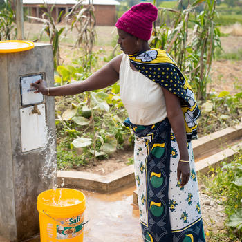 Community member Asha Kimoro uses her eWater token to collect water from a new distribution point, which is part of the WaterAid project. Sangara Village, Tanzania.